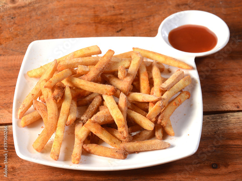 Garlic flavoured French fries served in a plate with tomato ketchup over a rustic wooden background, selective focus