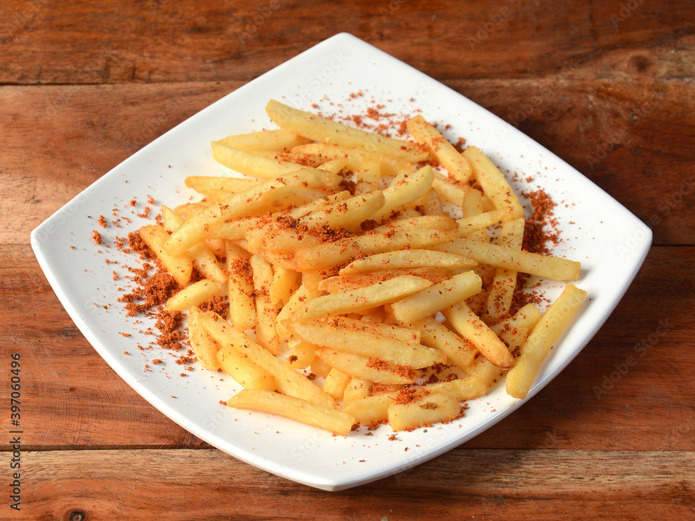 Tasty spicy Peri Peri French Fries served in a plate over a rustic wooden background, selective focus