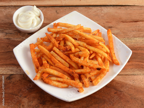 Tasty spicy Peri Peri French Fries with mayonnaise served in a plate over a rustic wooden background, selective focus