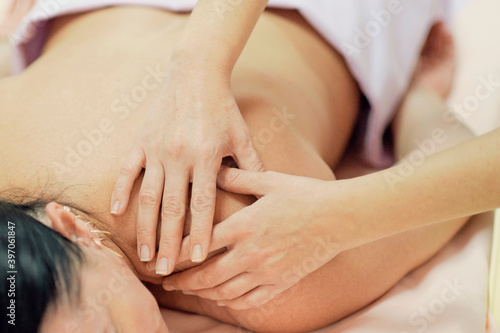 Physical Therapist Massaging the Back and Shoulder of a Female Patient. Over shoulder view of masseur performing deep tissue massage of womens back to release pain