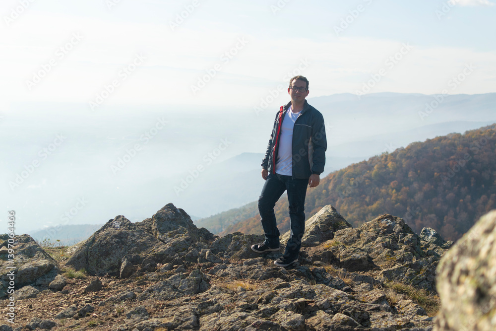 Young man standing on top of cliff in summer mountains at sunset and enjoying view of nature