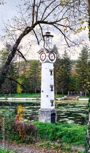 White clock tower in the middle of a blue artificial lake and surrounded by green and yellow vegetation