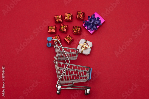 Supermarket cart and different sized christmas presents on red background