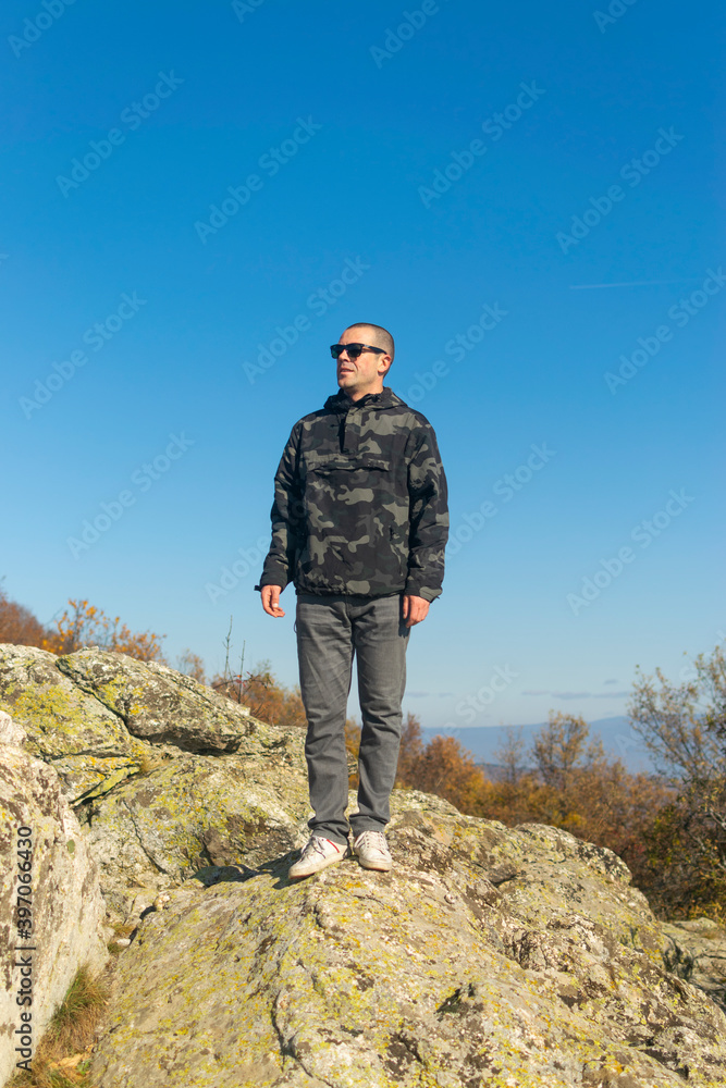 Young man standing on top of cliff in summer mountains at sunset and enjoying view of nature