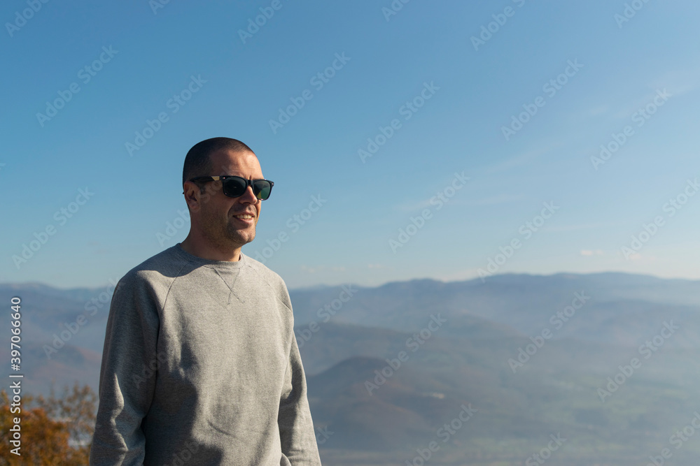 Young man standing on top of cliff in summer mountains at sunset and enjoying view of nature