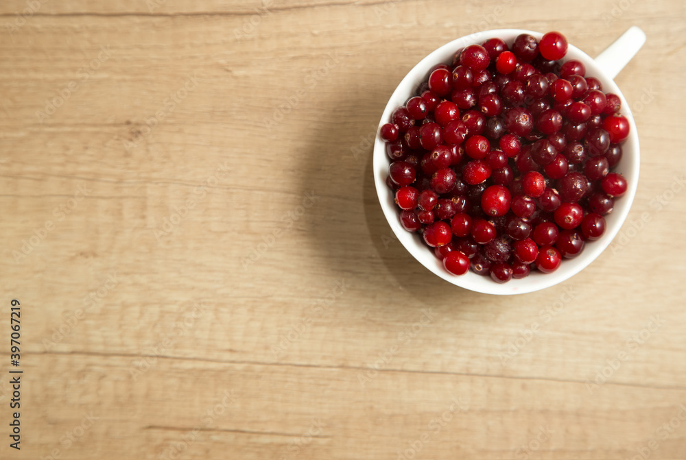 red cranberries in a white cup on a wooden background, flat lay red cranberries in a white cup on a wooden background, flat lay