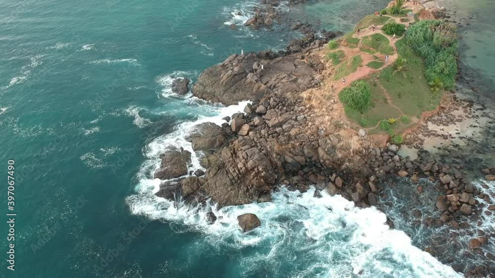 Top view of the small and green island of Mirissa in the middle of the sea which beats against the coastal flat rocks