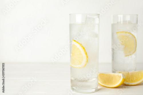 Soda water with lemon slices and ice cubes on white wooden table. Space for text