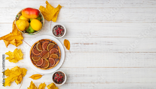 Pumpkin pie on a white wooden background. Yellow autumn leaves, apples and pears. Place for text.