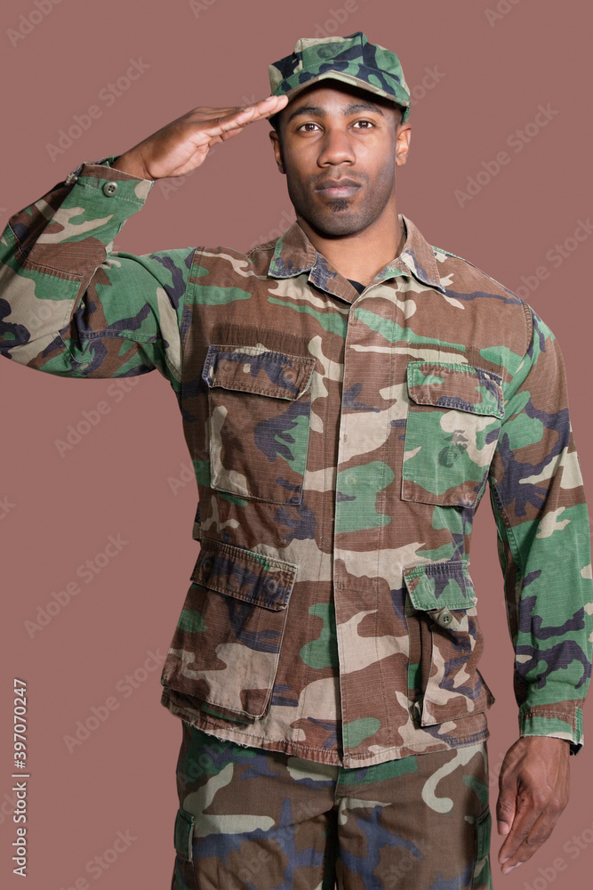 Fototapeta premium Portrait of a young African American US Marine Corps soldier saluting over brown background