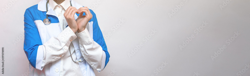 Young doctor smiles and shows a heart sign with his hands. White background. Isolated. Christmas and New Year concept. Portrait. Copy space. Place for text Young doctor smiles and shows a heart sign with his hands. White background. Isolated. Christmas and New Year concept. Portrait. Copy space. Place for text