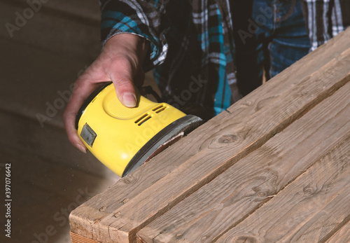 Man with checkered shirt sanding a pallet
