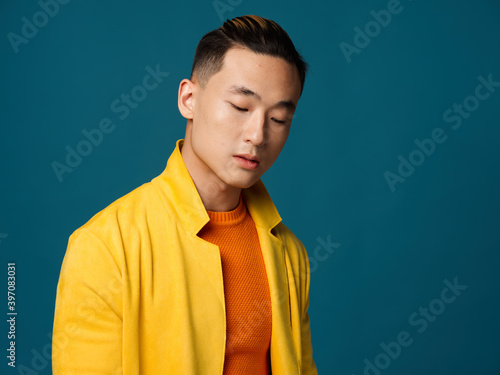 A man with closed eyes in a yellow jacket on a blue background close-up cropped view