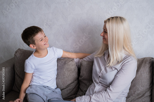 Blonde mom and teen son are sitting on the couch, looking at each other and smiling