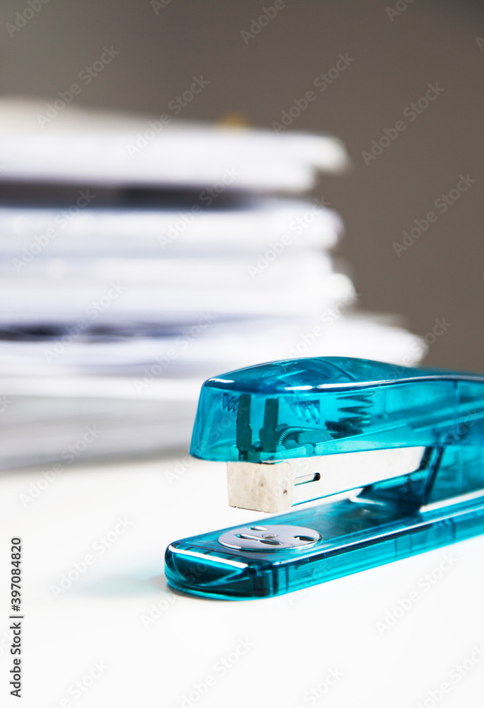 Stapler on white table with stack of papers in background Stapler on white table with stack of papers in background