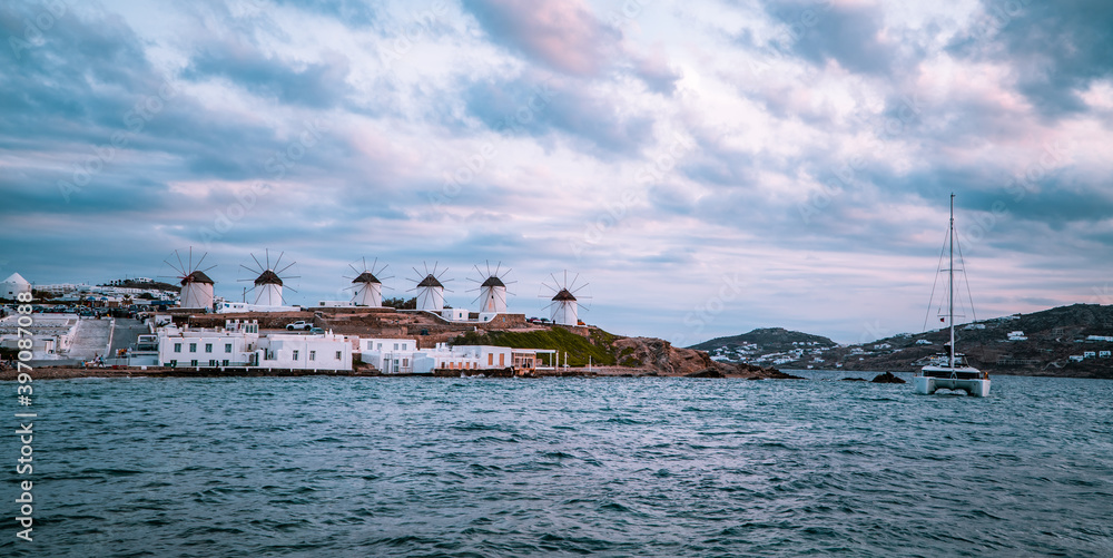 Panoramic sunset view of catamaran, windmills, and Aegean ocean in Mykonos Town (Chora) on the island of Mykonos, Cyclades
