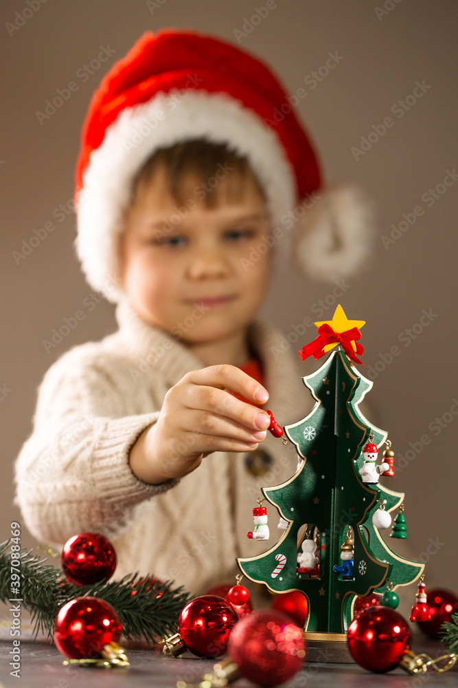 Boy in santa hat decorates wooden christmas tree