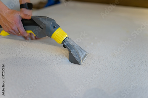 Employee of cleaning company cleans and disinfecting the mattress using a washing vacuum cleaner. Furniture dry cleaning process