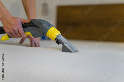 Employee of cleaning company cleans and disinfecting the mattress using a washing vacuum cleaner. Furniture dry cleaning process