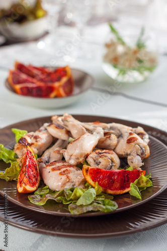 Grilled Frog Legs Garnished with Blood Orange Slices and Fresh Lettuce