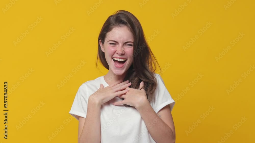 Excited laughing brunette young woman 20s years old in white t-shirt posing isolated on yellow color background in studio. People lifestyle concept. Pointing index finger on camera put hands on chest Excited laughing brunette young woman 20s years old in white t-shirt posing isolated on yellow color background in studio. People lifestyle concept. Pointing index finger on camera put hands on chest