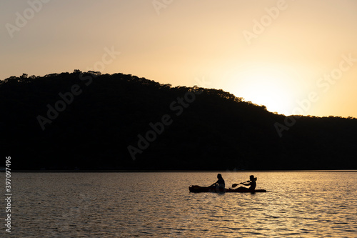 2 silhouettes in a canoe at sea at sunset
