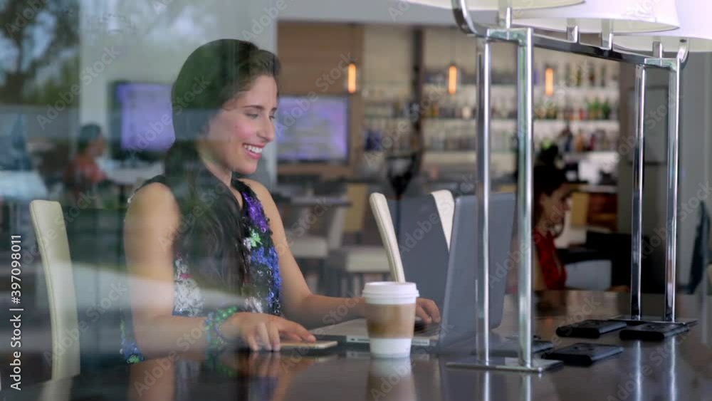 Hispanic woman using laptop and cell phone in cafe Hispanic woman using laptop and cell phone in cafe