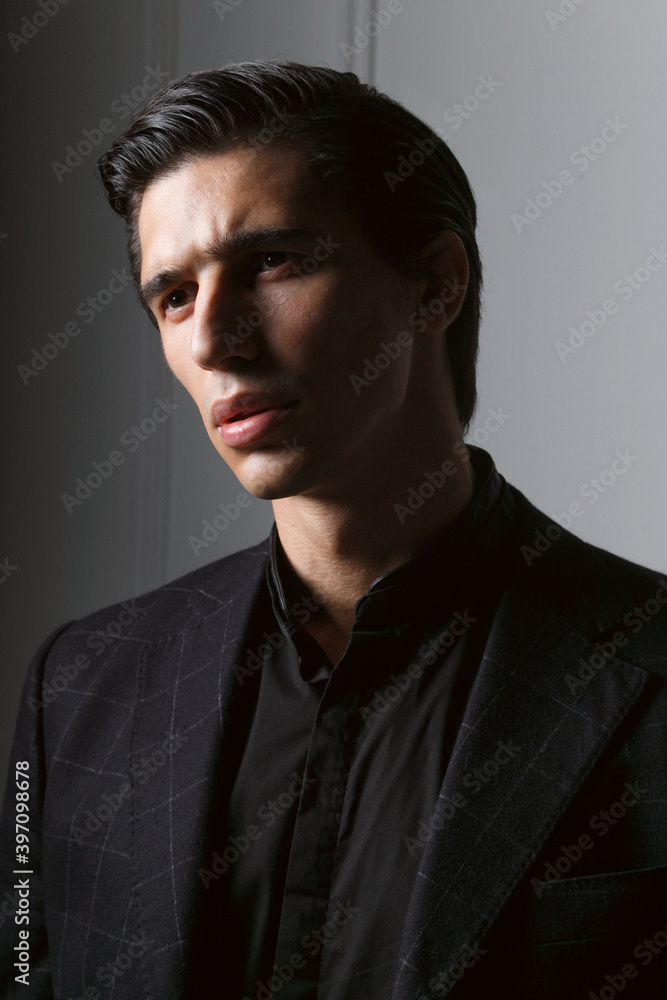 Fototapeta premium Closeup portrait of a handsome business man dressed in black suit against a dark grey background.