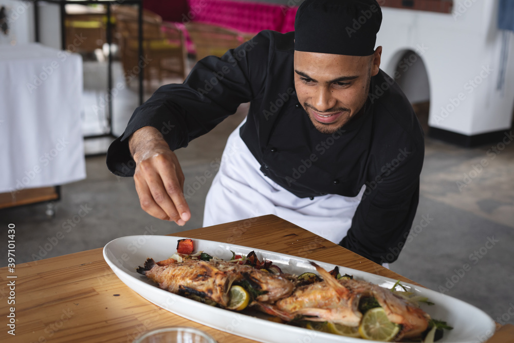Male middle eastern chef adding salt over roasted fish dish in food plate at restaurant kitchen Male middle eastern chef adding salt over roasted fish dish in food plate at restaurant kitchen