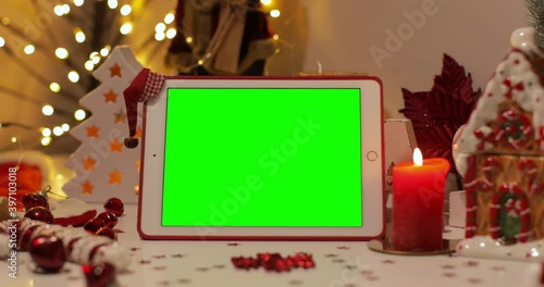 iPad Air tablet with pre-keyed green screen and Santa Claus hat on top standing in front of Christmas background. Easy to paste your content. Zoom in shot