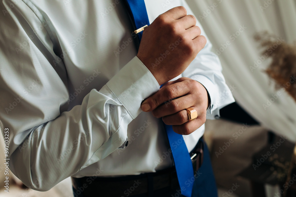 A businessman fastens a cufflink on his wrist watch, the cuff of the sleeve of a luxurious white shirt.
