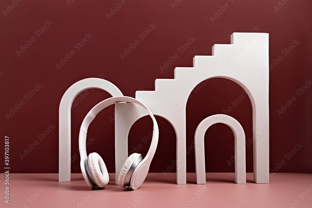 Studio with geometric objects, arch and white earphones. Exhibition Podium, stand, showcase on red pink background. Architectural background for advertising products