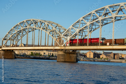 Red train crossing railway bridge over river Daugava