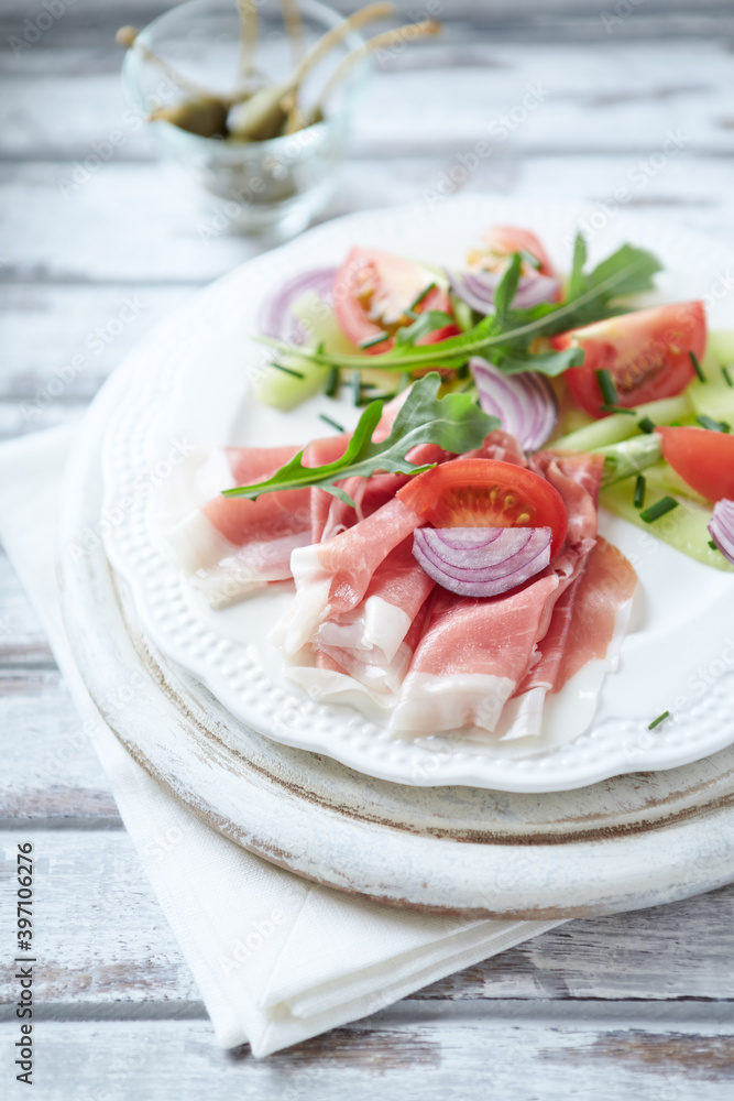 Plate of smoked ham with tomatoes and rocket. Bright wooden background.