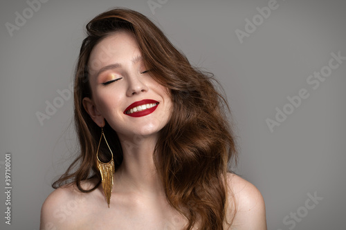 Portrait of a charming brunette with red lips on a gray background. Fashion hairstyle and makeup