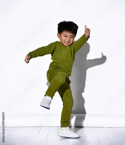 Fashion portrait of cute little kid boy in stylish green tracksuit dancing break against white studio wall. The concept of sports and healthy activities for the modern child.
