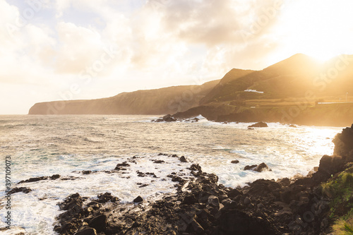 an ocean waves crushing into the rocks island blue water sunny day Atlantic ocean Sao Miguel island Portugal sunny morning sunshine daylight hills mountains shore 