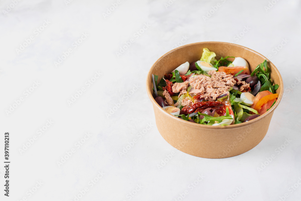 Fish diet salad with tuna, tomatoes, arugula on light background top view. Healthy lunch. Eco-friendly carton packaging, environment protection. Food delivery in disposable plate of craft paper. Fish diet salad with tuna, tomatoes, arugula on light background top view. Healthy lunch. Eco-friendly carton packaging, environment protection. Food delivery in disposable plate of craft paper.