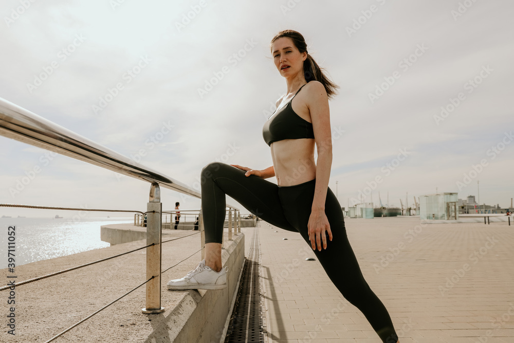 Sporty and happy woman stretching body after jogging, posing outdoor.