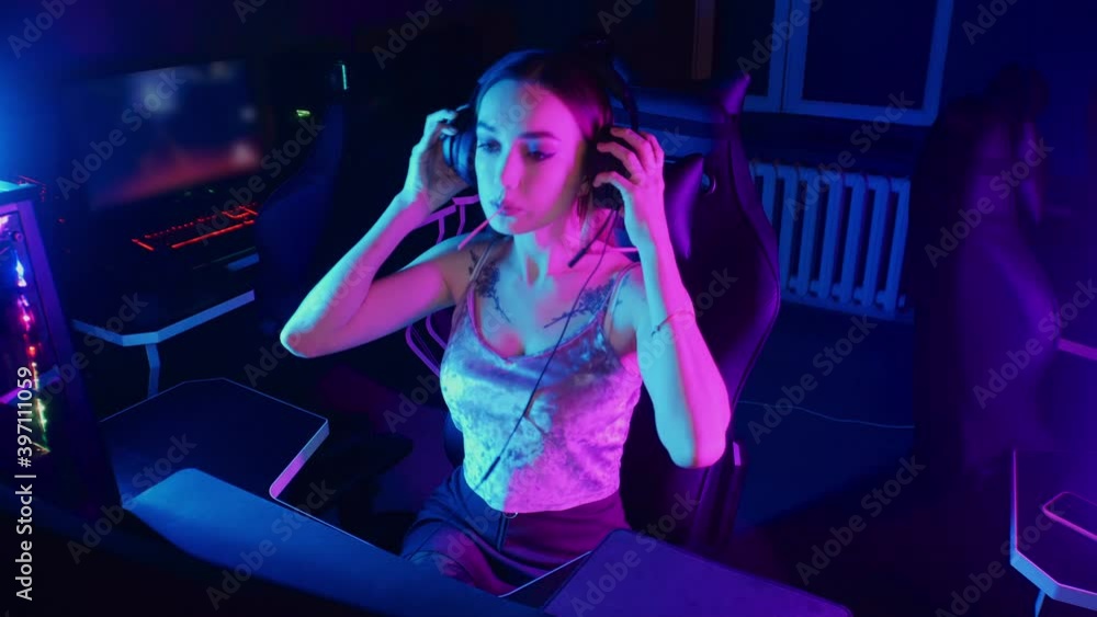 Gaming concept - young attractive gamer woman sits in the chair in neon gaming club and sucking a lollipop Gaming concept - young attractive gamer woman sits in the chair in neon gaming club and sucking a lollipop