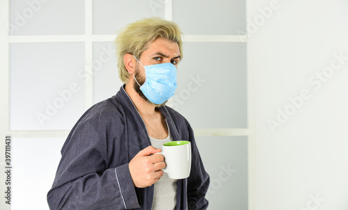 man drinks coffee in medical mask. morning at home on coronavirus self isolation. pandemic quarantine. Anti-virus mask. Masks to protect from virus. Man wears mask to protect from viral infection photo