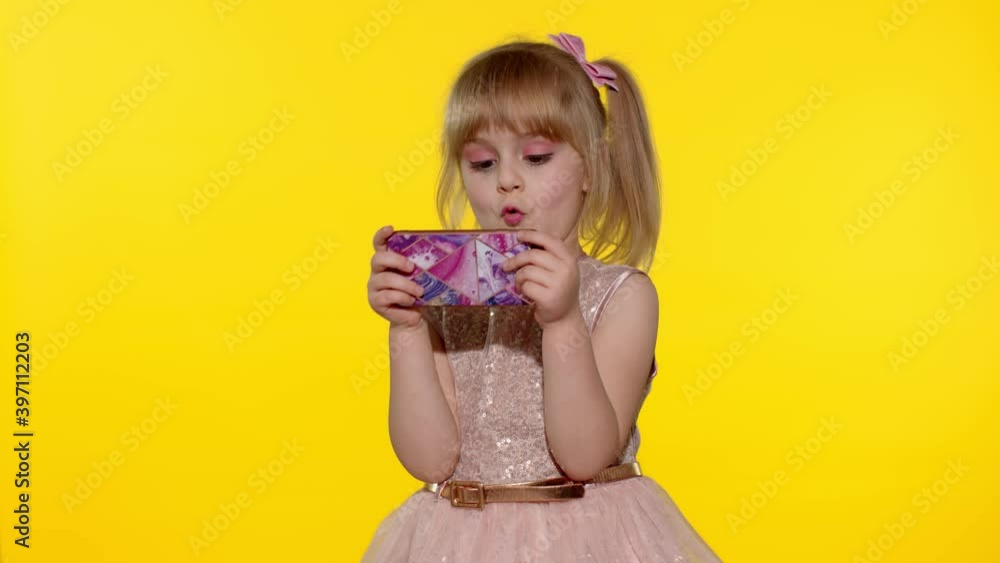 Little girl using smartphone. Portrait of child texting on smartphone. Kid enthusiastically playing games on mobile phone isolated on yellow background in studio. Technology for children. Slow motion Little girl using smartphone. Portrait of child texting on smartphone. Kid enthusiastically playing games on mobile phone isolated on yellow background in studio. Technology for children. Slow motion