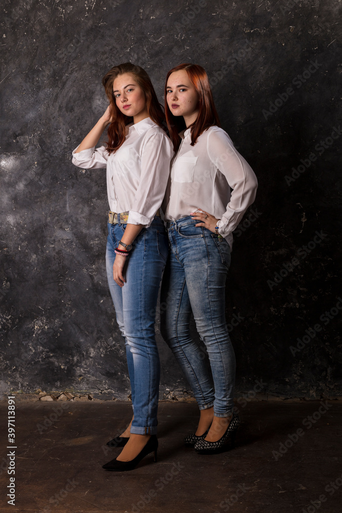 Beautiful teen girls dressed in white shirt and blue jeans standing close to each other