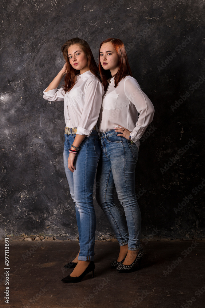 Beautiful teen girls dressed in white shirt and blue jeans standing close to each other Beautiful teen girls dressed in white shirt and blue jeans standing close to each other