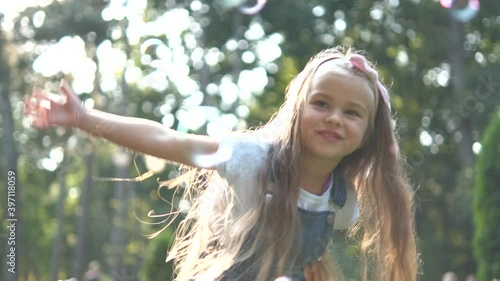 Little happy child girl cathing and bursting soap bubbles outdoors in summer. photo