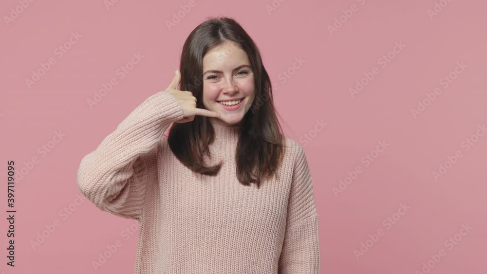 Cheerful brunette young woman 20s in pastel sweater isolated on pink background studio. People lifestyle concept. Pointing index finger on camera doing phone gesture like says call me back blinking Cheerful brunette young woman 20s in pastel sweater isolated on pink background studio. People lifestyle concept. Pointing index finger on camera doing phone gesture like says call me back blinking
