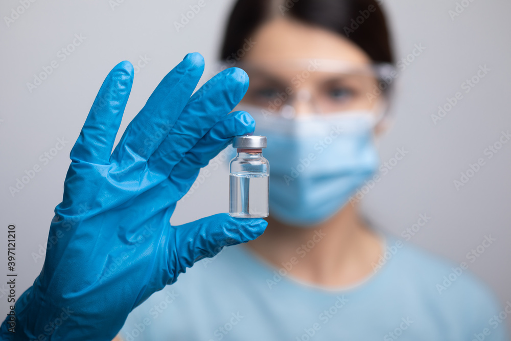 Doctor scientis in protective gloves and mask holding glass vial with injection liquid. Vaccination against influenza and coronavirus. Doctor scientis in protective gloves and mask holding glass vial with injection liquid. Vaccination against influenza and coronavirus.