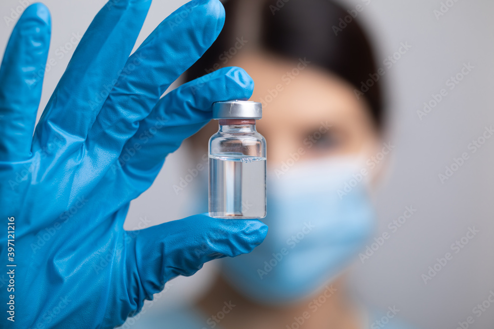 Doctor scientis in protective gloves and mask holding glass vial with injection liquid. Vaccination against influenza and coronavirus. Doctor scientis in protective gloves and mask holding glass vial with injection liquid. Vaccination against influenza and coronavirus.
