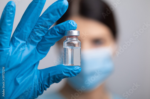 Doctor scientis in protective gloves and mask holding glass vial with injection liquid. Vaccination against influenza and coronavirus.