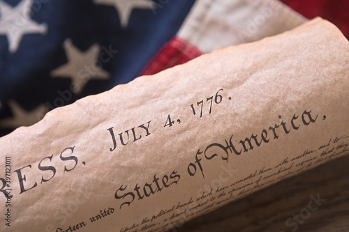 Independence Day July 4th Date on a copy of the Declaration of Independence with American flag in the background